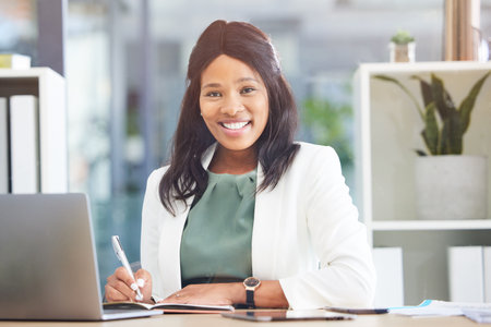 Office, portrait and black woman writing in notebook for business schedule, time management and calendar in Human Resources. Face of an HR corporate worker at her desk on laptop for career excellenceの写真素材