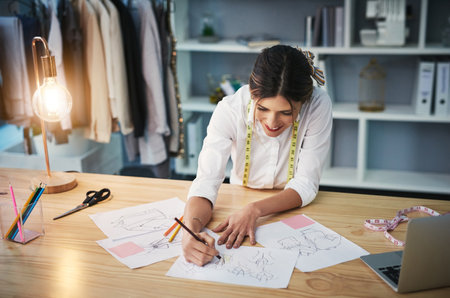 Shes always designing. High angle shot of an attractive young fashion designer working on her designs in her workshop.の写真素材