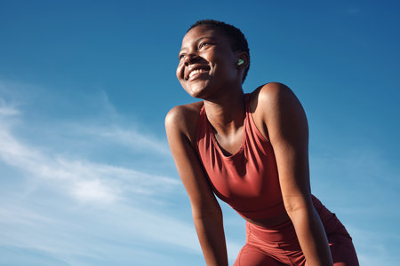 Fitness, black woman and happy athlete smile after running, exercise and marathon training workout. Blue sky, summer sports and run of a African runner breathing with happiness from sport outdoorの写真素材