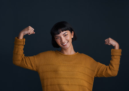 Im a woman, thats my superpower. Studio shot of an attractive young woman flexing her muscles against a dark background.の写真素材