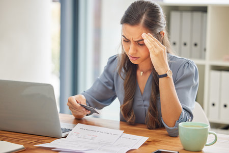 Stress, credit card or business woman with laptop confused with finance, burnout or budget depression in office. Document, bill or employee with headache for loan payment decline, debt anxiety or taxの写真素材