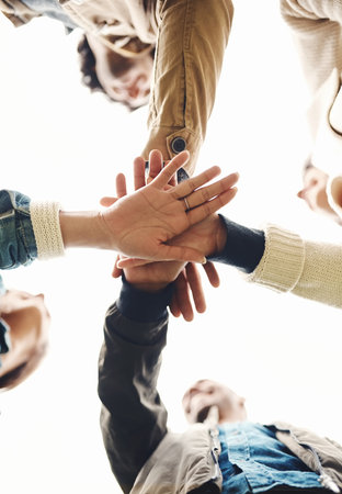 We make the best team. Low angle shot of a group of young friends forming a huddle with their hands together outside during the day.の写真素材