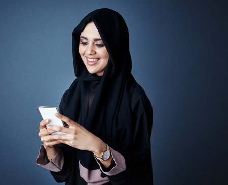 Doing business on the move. an attractive young businesswoman sending a text while standing against a dark background.の写真素材