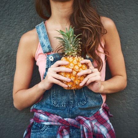 Only you and me mister pineapple. an unrecognizable young woman holding a pineapple while standing against a grey background.の写真素材