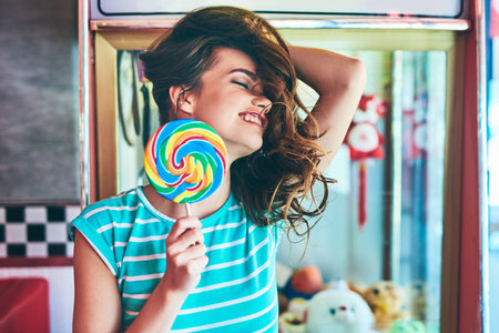 Shes having a sweet time. an attractive young woman eating a giant lollipop in a retro diner.の写真素材