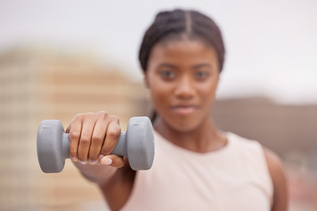 Fitness, dumbbell or black woman in a city training, workout or arm exercise for strong muscles or growth. Blurry, motivation or healthy African girl exercising for body development on a rooftopの写真素材