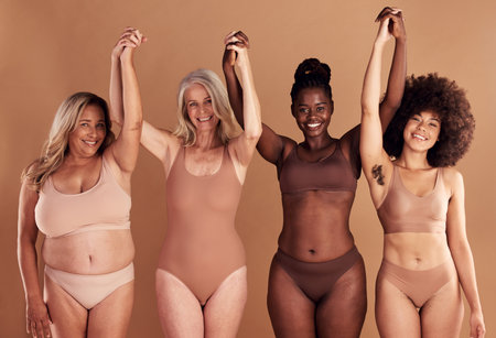 Beauty, diversity and natural with woman friends in studio on a beige background with their hands raised in celebration. Wellness, underwear and real with a model female group standing togetherの写真素材