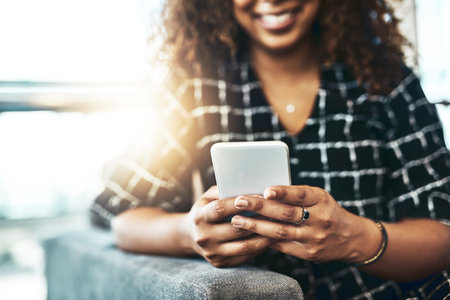 Connect smart and receive the best results. an unrecognizable businesswoman using a smartphone while sitting on a couch in a modern office.の写真素材