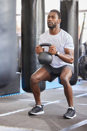 Black man, gym and kettlebell for squat exercise, weightlifting workout or muscle growth training. African bodybuilder, wellness trainer and metal weights for strong legs, body development or healthの写真素材