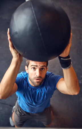 Got to keep the eyes on the prize. High angle shot of a handsome young man working out with a medicine ball in the gym.の写真素材
