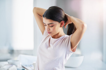 Its a ponytail kinda day. a beautiful young woman styling her hair in the bathroom at home.の写真素材