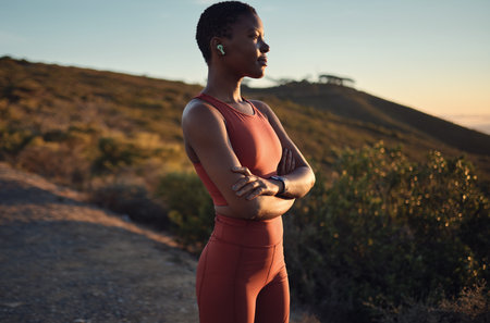 Thinking, vision and fitness with a sports black woman standing arms crossed outdoor in nature. Exercise, training and workout with a female athlete listening to music during cardio or enduranceの写真素材