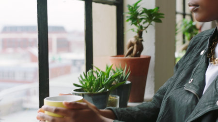 Black woman, coffee and a designer thinking while looking out window in a modern office at a startup company. Face of a calm young female with glasses looking for idea or inspiration while on a breakの写真素材