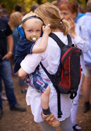Protecting his sensitive little ears at the festival. a toddler being carried by his mother at an outdoor festival.の写真素材