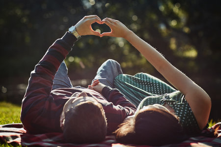 True love is everything. a young couple lying together on the grass and making a heart gesture with...