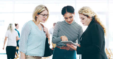 Filling them in. three corporate businesswomen standing in a huddle with digital tablets in hand.の写真素材