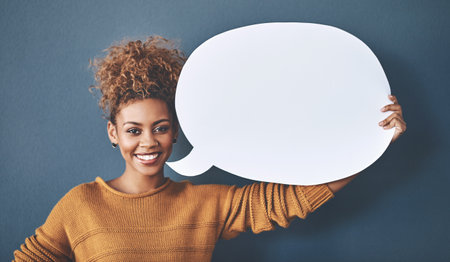 Could I have everyones attention please. Studio shot of a young woman holding a speech bubble against a grey background.の写真素材