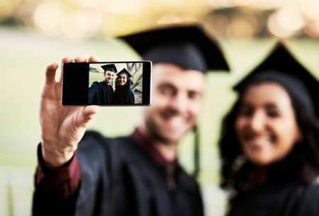 Look who just graduated. two students taking a selfie together on graduation day.