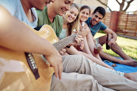 Playing them a song. a young man playing guitar while enjoying a few drinks with his friends outside...