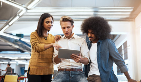 Getting some much needed input. three young businesspeople looking at a tablet in their office.