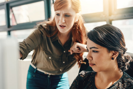Work as one, get things done. two young businesswomen using a computer together in a modern office.の写真素材