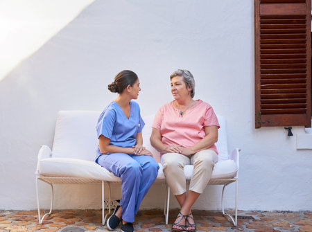 Out for some fresh air and a good chat. a caregiver chatting to a senior patient outside.の写真素材