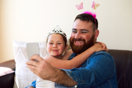 No makeover is complete without a selfie. an adorable little girl playing dress up and taking selfies with her father at home.の写真素材
