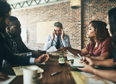Are we done with this meeting yet. an overwhelmed businessman holding his head while his colleagues...
