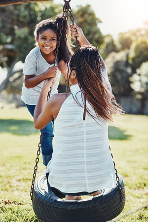 Its going to be a day of nonstop fun. a mother pushing her daughter on a swing at the park.の写真素材