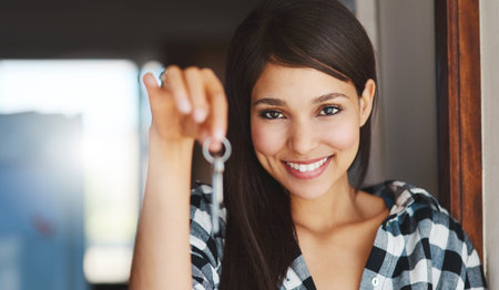 Guess whos got a new address. Portrait of a happy young woman holding the key to her new home.の写真素材
