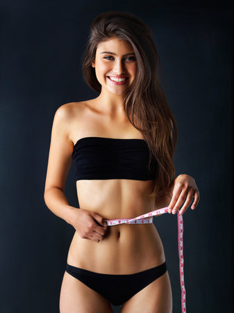 No time to waist. a beautiful young woman posing against a dark background.の写真素材