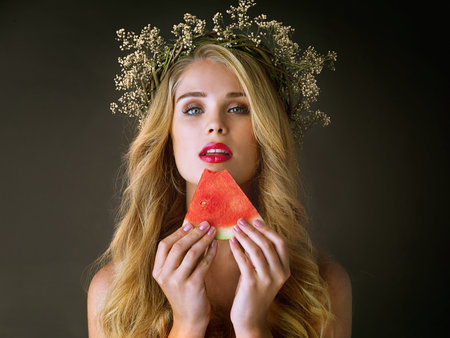 Seductively sweet. Studio shot of a gorgeous young woman eating a slice of watermelon against a dark background.の写真素材