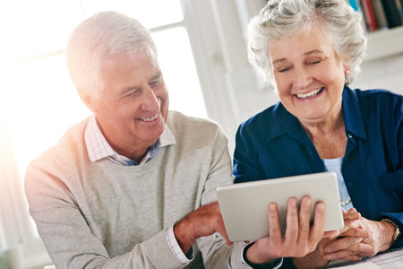 Discovering all the tricks to technology. a senior couple using a digital tablet together at home.の写真素材