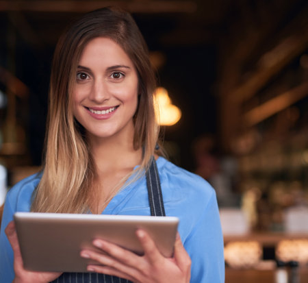 Managing my business online. Cropped portrait of an attractive young woman using a digital tablet in her coffee shop.の写真素材