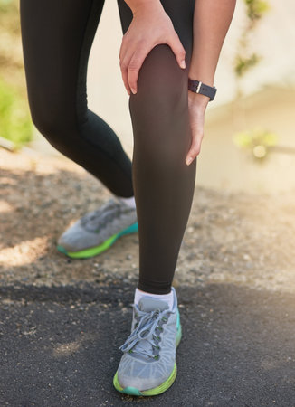 Feeling the effects of a strenuous run. an unrecognizable young woman holding her knee in pain during her morning run.の写真素材