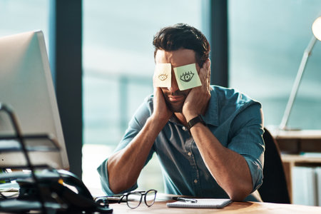 Thats it, Im done. a tired young businessman working at his desk with adhesive notes covering his eyes.の写真素材