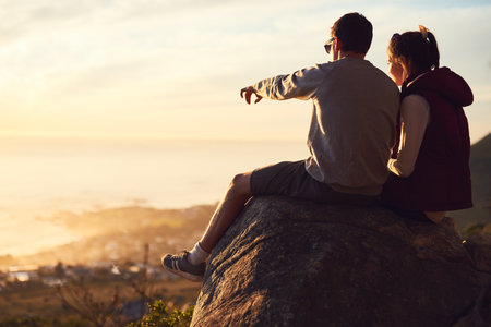 I can see your house from here. Rearview shot of a young couple admiring the view from the top of a mountain.の写真素材