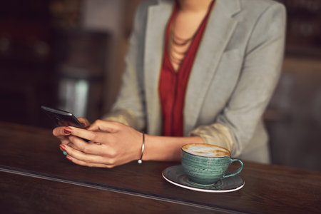 Connectivity with a cup of comfort on the side. an unidentifiable woman texting on a cellphone in a cafe.の写真素材