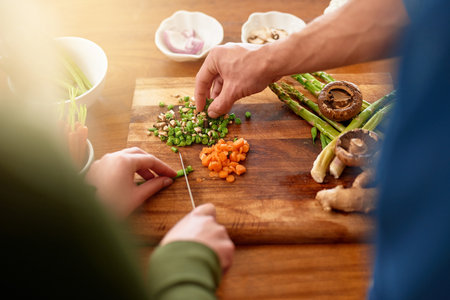 They put love into every meal. Over the shoulder shot of a young couple chopping up ingredients together at their kitchen counter for dinner.の写真素材