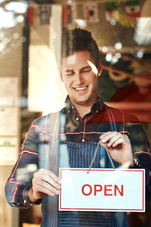 Youre the first customer for the day. Closeup shot of a young man hanging up an open sign in a shop...