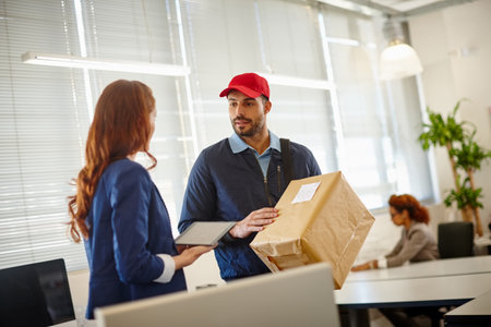 I have a package for an employee of yours. a young woman receiving a package from a deliveryman at her office.の写真素材