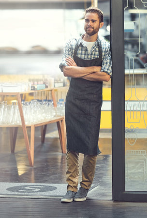 His doors are open for business. a confident young man working standing in the doorway of his store.の写真素材