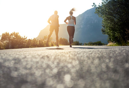 There are simply no shortcuts in the long run. Low angle shot of two people running on a tarmac road.の写真素材