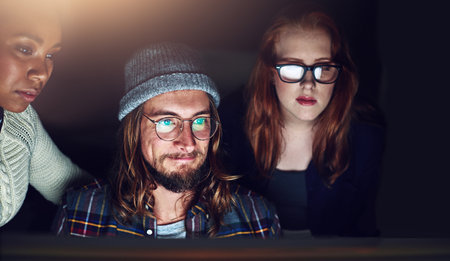 He has no problem working under pressure. a business team looking at a computer screen together on a night shift at work.の写真素材
