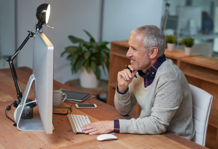 Putting on a few final touches to his project. a smiling mature businessman working on a computer in...