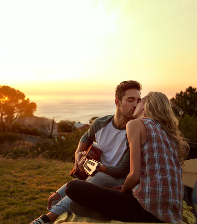Out on a romantic roadtrip. a young man playing guitar for his girlfriend on a roadtrip.の写真素材