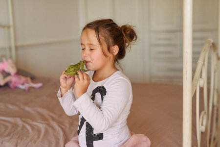 Maybe itll turn into a little prince. a little girl kissing a toy frog at home.の写真素材