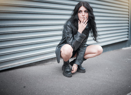 Punk, emo and woman smoking a cigarette in the street of an urban city in Canada in an edgy black...
