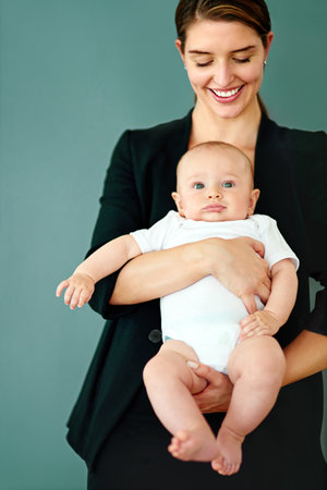 Family and business, she makes it work. Studio shot of a successful young businesswoman carrying her adorable baby boy.の写真素材
