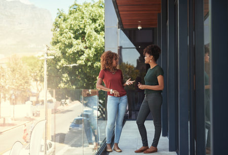 Communication in the workplace is important. two businesswomen chatting outside on a balcony.の写真素材